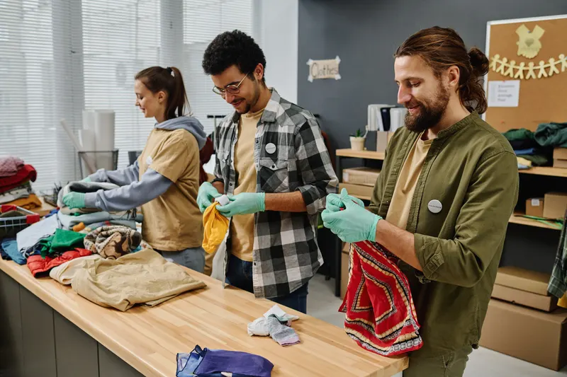 Des bénévoles d'une association trient des vêtements autour d'une table.