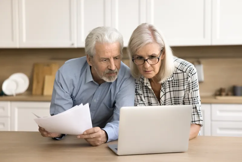 Un couple de retraités relit des documents à la table de la cuisine.