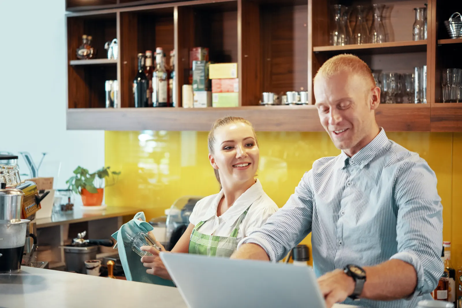 Une gérante de café consulte son ordinateur avec son employée derrière le comptoir.