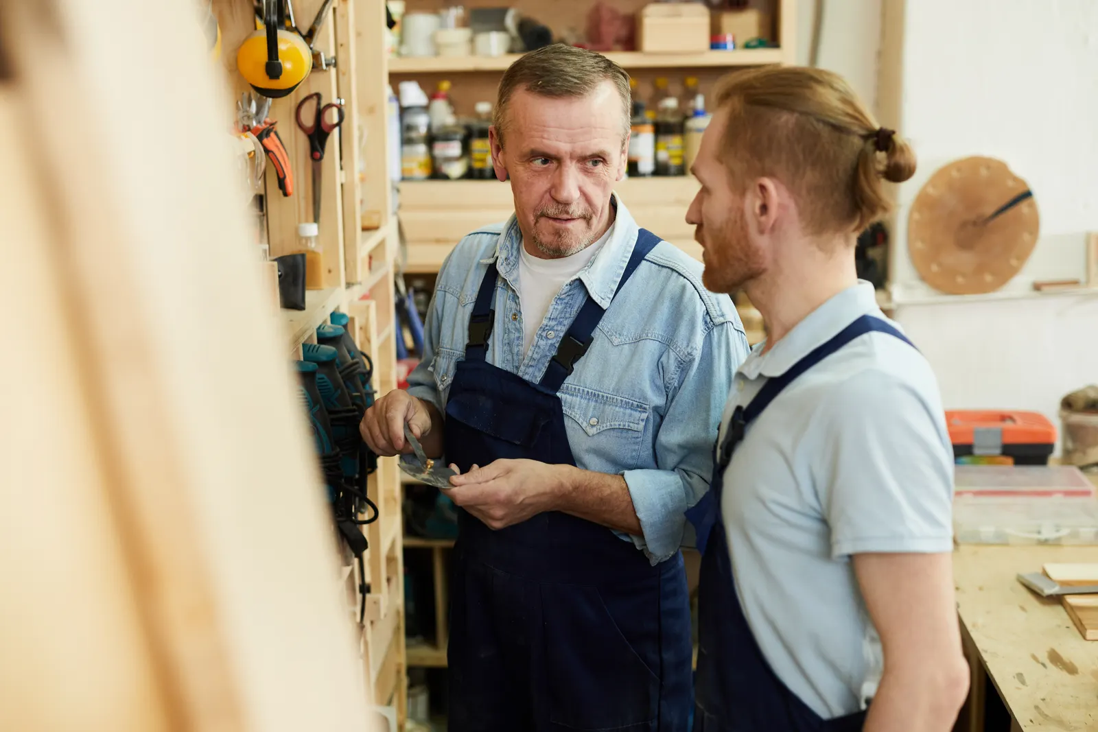 An experienced carpenter talks with his apprentice in the workshop.